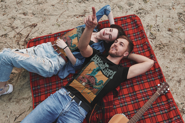 Couple laying on a blanket at festival, wearing black Absolem Smoke Shop tees from Alice in Wonderland